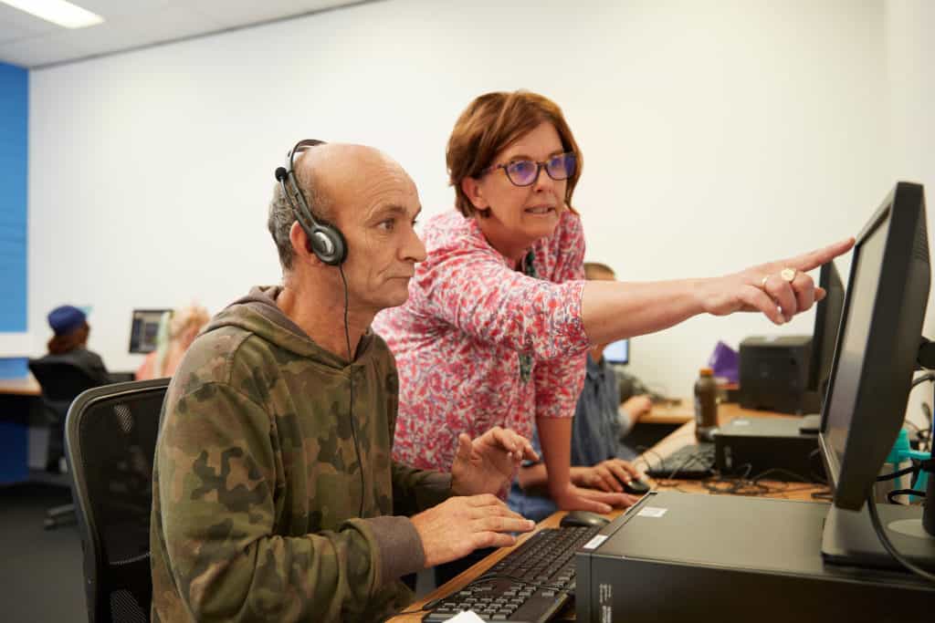 Teacher helping mature-aged male student at a computer.